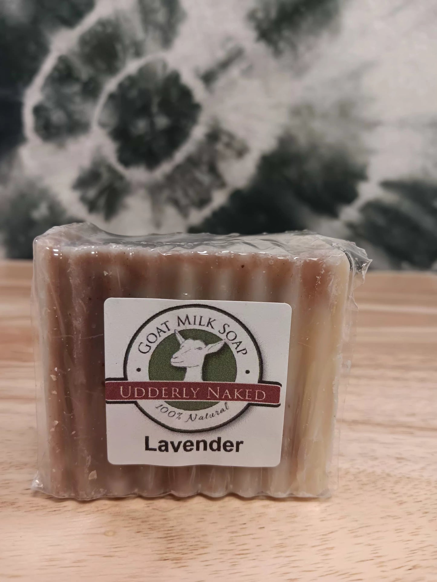 Bar of lavender goat milk soap with a clear plastic wrap on a wooden surface.