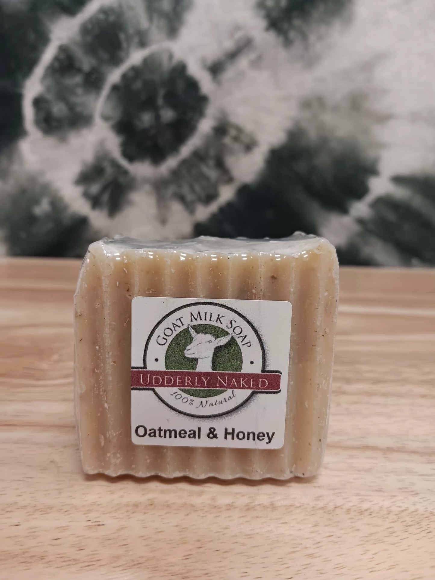 Bar of goat milk soap labeled 'Udderly Naked' with an oatmeal and honey scent on a wooden surface.