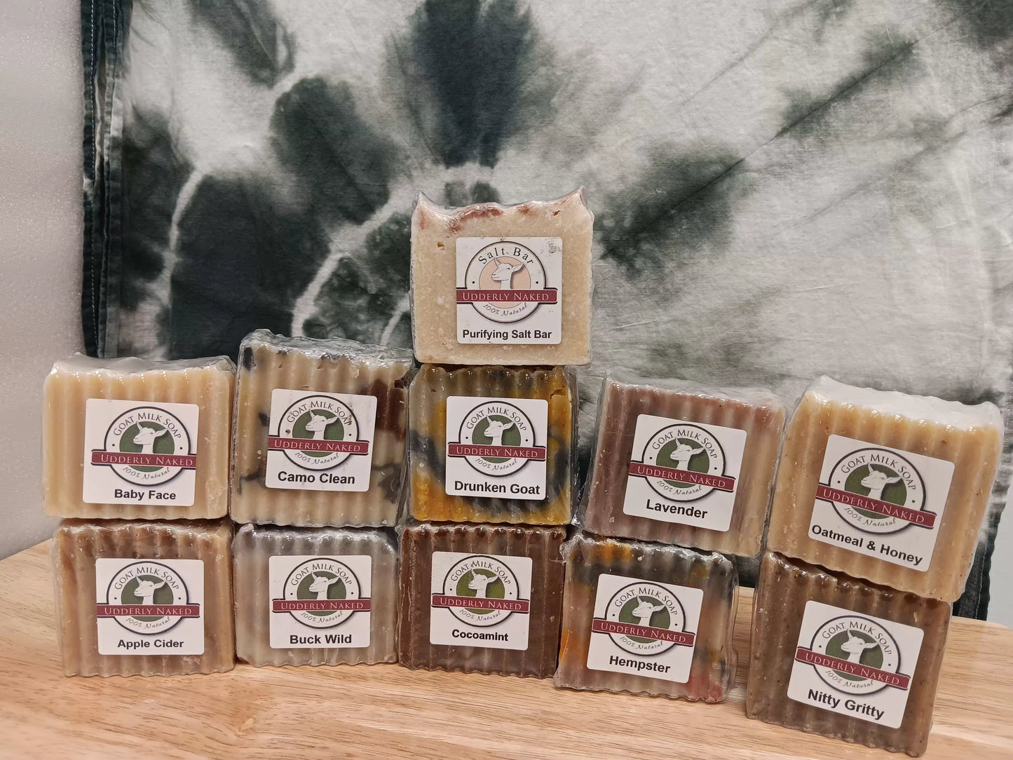 Assorted soap bars with labels on a wooden surface and tie-dye background